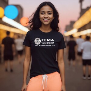 A smiling woman wearing a black short-sleeved t-shirt with a parody FEMA evacuation plan graphic.