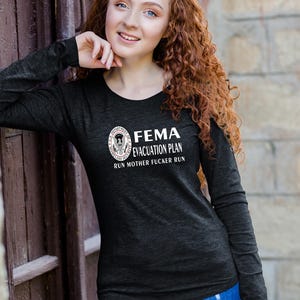 A woman with curly red hair wearing a black long-sleeve t-shirt featuring the FEMA evacuation plan text and seal.