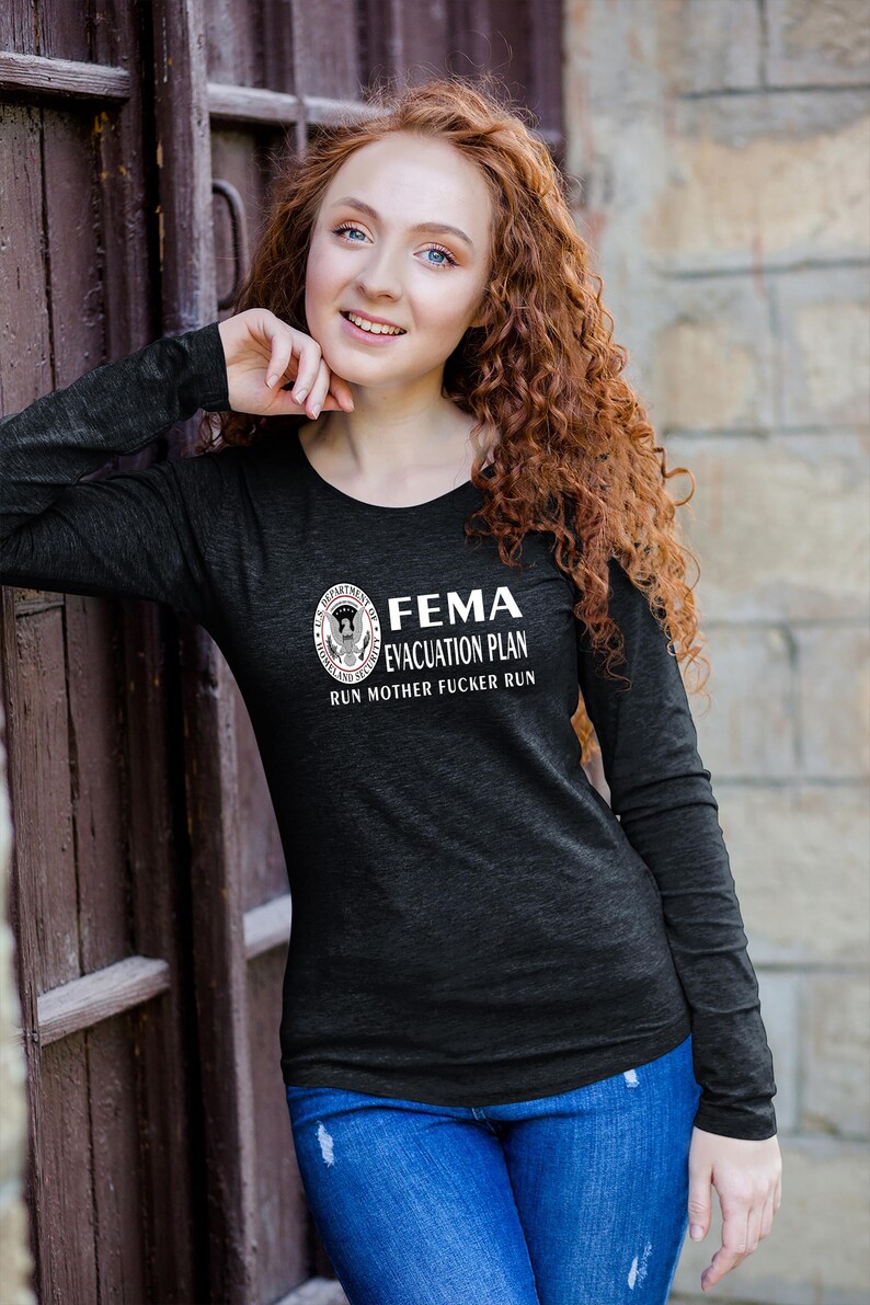 A woman with curly red hair wearing a black long-sleeve t-shirt featuring the FEMA evacuation plan text and seal.