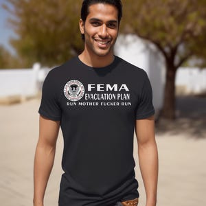 A smiling man wearing a black short-sleeved t-shirt with a printed FEMA evacuation plan slogan.