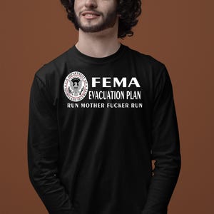 A man with curly dark hair wearing a black long-sleeve shirt with a FEMA evacuation plan graphic.