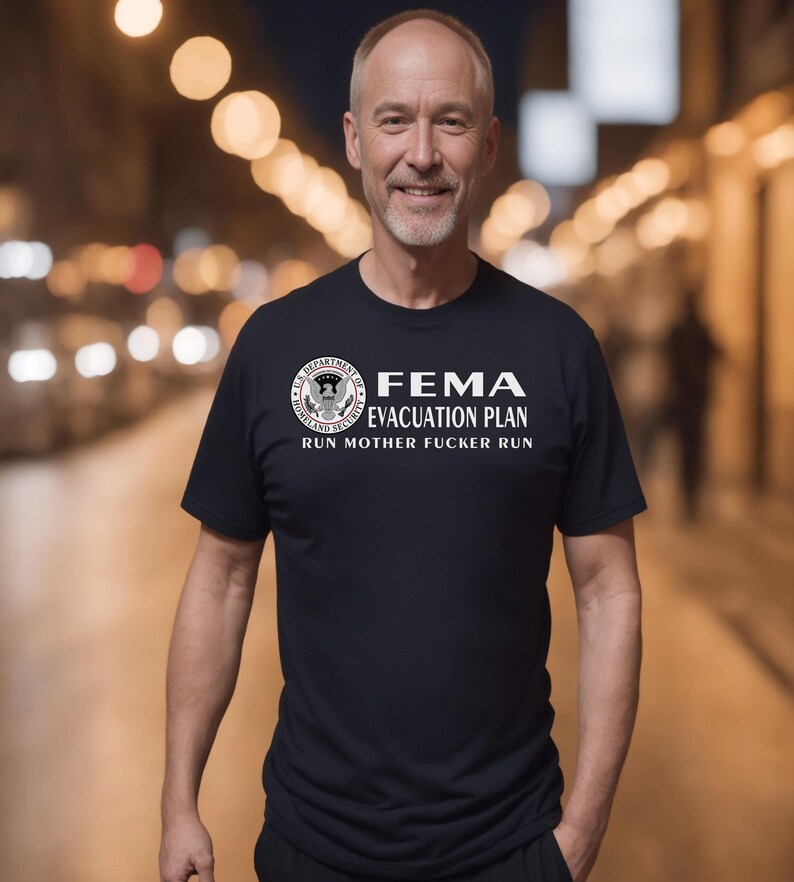 A mature man smiling outdoors in a black t-shirt displaying a humorous FEMA emergency design.