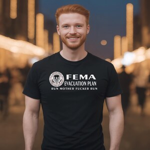 A smiling red-haired man wearing a black crewneck t-shirt featuring a FEMA evacuation plan design.