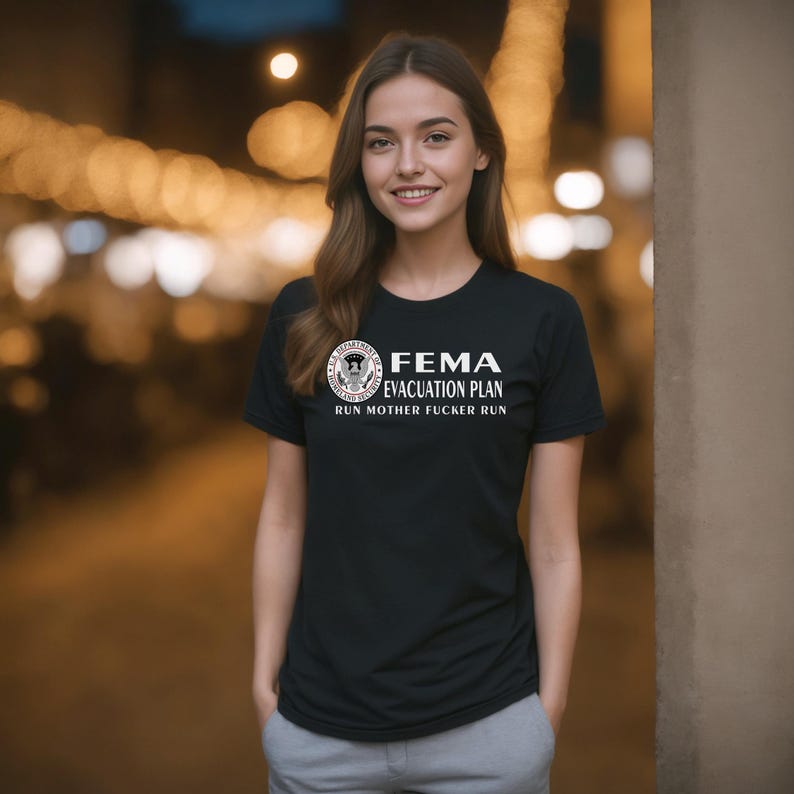 A woman standing outdoors wearing a black t-shirt with a parody FEMA evacuation plan graphic.