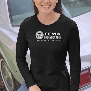 A smiling woman in a black long-sleeve shirt with a FEMA evacuation plan print posing near a car.