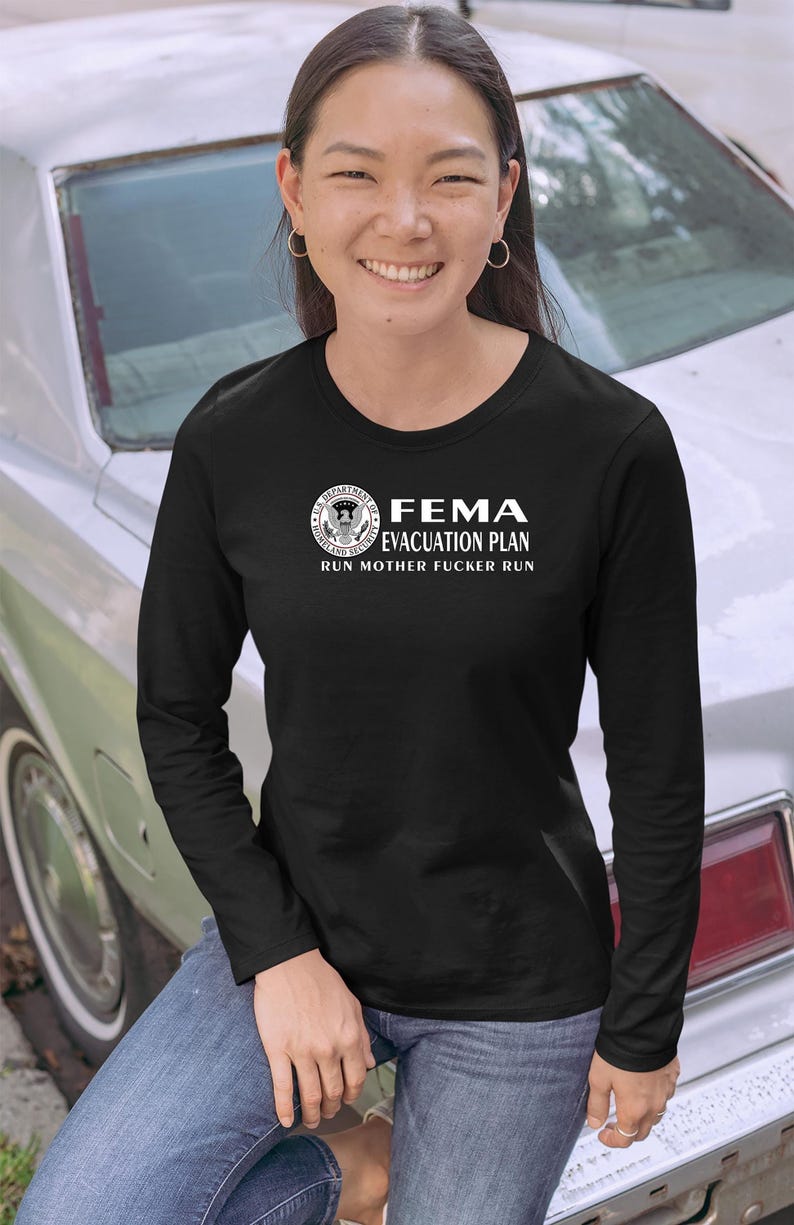 A smiling woman in a black long-sleeve shirt with a FEMA evacuation plan print posing near a car.