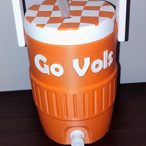 May include: Orange and white insulated drinks cooler with a handle and straw. The cooler has the words "Go Vols" printed on the side. The lid features a checkered pattern.