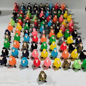 May include: A collection of miniature bird figurines in various colors, including black, gold, red, pink, blue, orange, yellow, and green. The figurines are arranged on a white surface, showcasing their diverse hues and designs.