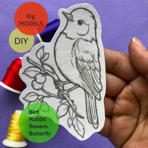 Könnte beinhalten: Eine Schwarzweiß-Zeichnung eines Vogels, der auf einem Ast mit Blättern und Beeren sitzt. Das Bild ist auf weißem Hintergrund und von bunten Stickgarnen umgeben.