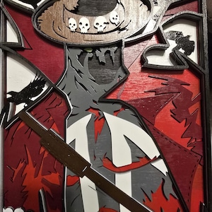 以下が含まれることがあります： 幅広の帽子、長いコート、剣を持ったキャラクターを描いた木製の壁飾り。キャラクターは、帽子にドクロのモチーフをあしらった、暗いスタイリッシュなポーズをとっている。この作品は、重ねられた木で作られており、赤、黒、白の色合いで塗られている。