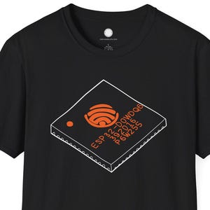 Könnte beinhalten: Schwarzes T-Shirt mit einer weißen und orangefarbenen Grafik eines Computerchips. Das Chip-Design enthält den Text "ESP32-DOWDQQ" und andere technische Details. Das Shirt hat einen Rundhalsausschnitt und kurze Ärmel.