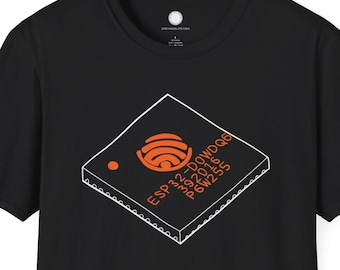 Puede incluir: Camiseta negra con un gráfico blanco y naranja de un chip de computadora. El diseño del chip incluye el texto "ESP32-DOWDQQ" y otros detalles técnicos. La camiseta es de cuello redondo y manga corta.