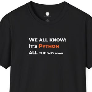May include: Black t-shirt with white and orange text that reads "WE ALL KNOW: IT'S PYTHON ALL THE WAY DOWN". The shirt is a short-sleeved crew neck.
