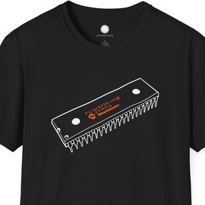 Könnte beinhalten: Schwarzes T-Shirt mit einer weiß-orangenen Grafik eines Computerchips. Das Chip-Design enthält den Text "Intel" und andere technische Details. Das Shirt ist kurzärmlig und hat einen Rundhalsausschnitt.