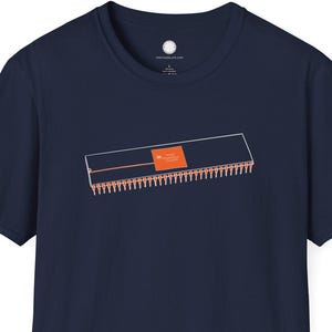 Op de afbeelding: Marineblauw T-shirt met een oranje en witte afbeelding van een computerchip. Het ontwerp is gecentreerd op de voorkant. Het shirt heeft korte mouwen en een ronde hals.