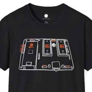 May include: Black t-shirt with a white and orange circuit board graphic. The design includes the word "READY" and other text. The shirt is a short-sleeved crew neck.