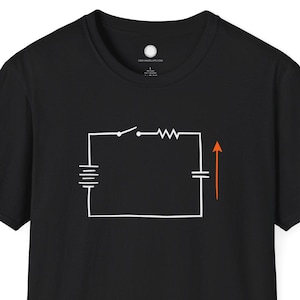 May include: Black t-shirt featuring a white schematic diagram of an electrical circuit. The diagram includes a battery, switch, resistor, and capacitor with an orange arrow indicating current flow. A simple, yet educational design.