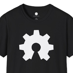Może przedstawiać: Czarny t-shirt z dużym, białym nadrukiem koła zębatego pośrodku. Projekt koła zębatego zawiera symbol open source pośrodku. Koszulka ma krótkie rękawy i okrągły dekolt.