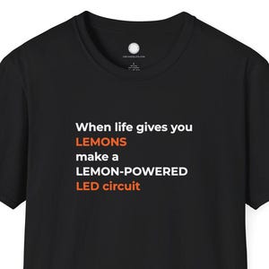 May include: Black t-shirt with the text "When life gives you LEMONS make a LEMON-POWERED LED circuit" in white and orange. The shirt has a crew neck and short sleeves. The shirt is made of a soft material.