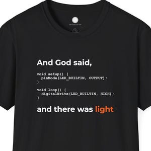Könnte beinhalten: Schwarzes T-Shirt mit dem Text "And God said, and there was light" in Weiß und Orange, gestaltet wie Computercode. Das Shirt hat einen Rundhalsausschnitt und kurze Ärmel.