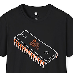 May include: Black t-shirt featuring a white and orange graphic of a computer chip. The chip design includes the text "CSG 8581R5 6692 25". The shirt is a classic crew neck style.