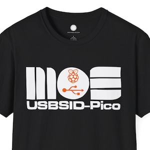 May include: Black t-shirt with a white and orange graphic. The graphic includes the word "MOE", a raspberry icon, a USB symbol, and the words "USBSID-Pico". The t-shirt has a crew neck and short sleeves.