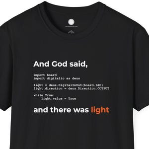 Może przedstawiać: Czarny t-shirt z okrągłym dekoltem z białym tekstem: "I rzekł Bóg, ... i nastała światłość". Tekst jest sformatowany jak kod. Fraza "i nastała światłość" jest czerwona.