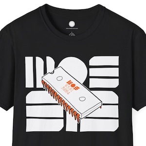 May include: Black t-shirt with a white graphic design featuring the word "MOS" and a stylized computer chip with orange details. The shirt has a crew neck and short sleeves.