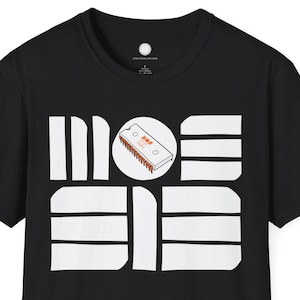 Peut inclure: T-shirt noir avec un motif graphique blanc. Le motif présente le mot "MODE" dans une police stylisée, avec un dessin de cassette au centre. Le t-shirt a un col rond et des manches courtes.