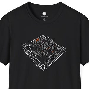 May include: Black t-shirt with a white and orange circuit board graphic. The design is positioned centrally. The shirt has a crew neck and short sleeves. The fabric appears to be cotton.