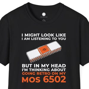 Puede incluir: Camiseta negra con el texto "I MIGHT LOOK LIKE I AM LISTENING TO YOU BUT IN MY HEAD I'M THINKING ABOUT GOING RETRO ON MY MOS 6502". El diseño incluye un chip de computadora blanco y naranja.