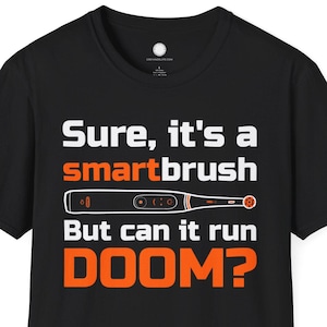 May include: Black t-shirt with white and orange text that reads "Sure, it's a smartbrush. But can it run DOOM?" The design includes an illustration of a toothbrush.