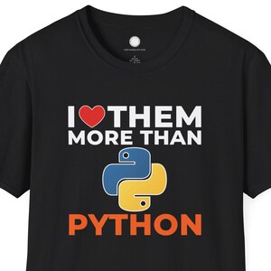 Puede incluir: Camiseta negra con el texto "I ❤️ THEM MORE THAN PYTHON". El diseño incluye un corazón rojo y un logotipo de Python azul y amarillo. Una camiseta informal para programadores y entusiastas de la codificación.