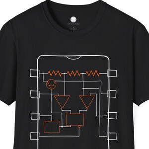 May include: Black t-shirt with a white and orange circuit diagram design. The graphic features rectangular and triangular shapes, lines and zigzags, creating a technical aesthetic. The shirt has a crew neck and short sleeves.