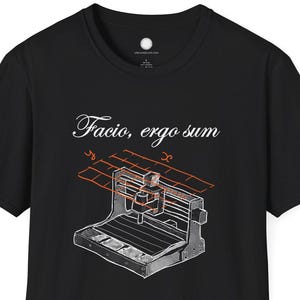 Pode incluir: Camiseta preta com uma ilustração detalhada de uma máquina CNC com detalhes em laranja e cinza. A frase latina "Facio, ergo sum" está impressa acima. Gola redonda clássica.