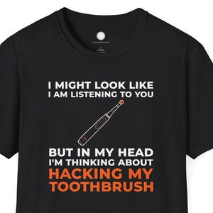 Könnte beinhalten: Schwarzes T-Shirt mit weißem und orangefarbenem Text: „I MIGHT LOOK LIKE I AM LISTENING TO YOU BUT IN MY HEAD I'M THINKING ABOUT HACKING MY TOOTHBRUSH.“ Eine Zahnbürstengrafik ist ebenfalls enthalten.