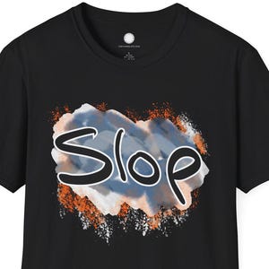 May include: Black t-shirt featuring the word "Slop" in a stylized, handwritten font. The word is set against a backdrop of blue, orange, and white brushstrokes, creating a bold graphic design. The shirt is a classic crew neck.