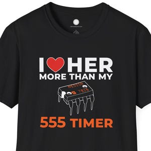 Pode incluir: T-shirt preta com o texto "I ❤️ HER MORE THAN MY 555 TIMER". O design inclui um coração vermelho e um gráfico de um circuito integrado 555.
