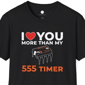 Pode incluir: T-shirt preta com o texto "I ❤️ YOU MORE THAN MY 555 TIMER". O design inclui um coração vermelho e uma ilustração de um circuito integrado 555 timer.