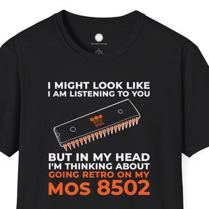 Puede incluir: Camiseta negra con texto blanco y naranja. El texto dice "I MIGHT LOOK LIKE I AM LISTENING TO YOU BUT IN MY HEAD I'M THINKING ABOUT GOING RETRO ON MY MOS 8502". También se incluye un gráfico de un chip de computadora.