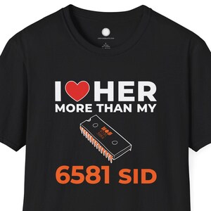 May include: Black t-shirt with the text "I ❤️ HER MORE THAN MY 6581 SID". The design includes a red heart and an illustration of a computer chip. The text and graphic are in white and orange.