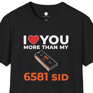 May include: Black t-shirt with the text "I ❤️ YOU MORE THAN MY 6581 SID". The design includes a red heart, white text, and an orange and brown illustration of a 6581 SID chip.