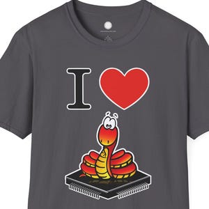 Op de afbeelding: Donkergrijs T-shirt met een cartoon slangenontwerp. Het ontwerp bevat een rood hart, de letter "I" en een geel en rode slang op een printplaat. De tekst op het shirt luidt "I ♥".