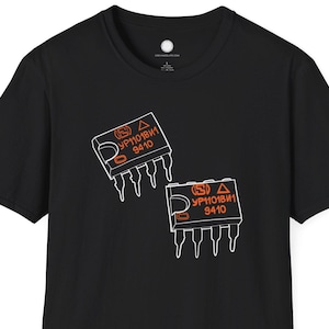 Può includere: T-shirt nera con due grafiche di circuiti stampati arancioni e bianchi. Ogni grafica presenta il testo "YP10181" e "9410". La maglietta è a maniche corte e girocollo.
