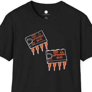 Può includere: T-shirt nero con due grafiche di circuiti stampati arancioni e bianchi. Ogni grafica riporta la scritta "YP1018W1 9410". La maglietta è a girocollo e maniche corte.