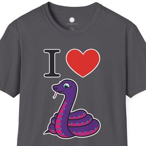 Może przedstawiać: Ciemnoszara koszulka z nadrukiem fioletowego węża z różowymi akcentami, czerwonym sercem i napisem "I <3". Wąż ma biały kontur i uśmiechniętą twarz.
