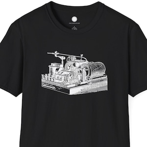 Puede incluir: Camiseta negra con una ilustración blanca detallada de una máquina industrial vintage. El diseño está centrado en la parte delantera, mostrando intrincados componentes mecánicos. La camiseta tiene un cuello redondo clásico y mangas cortas.