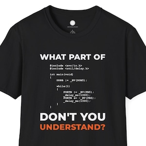 May include: Black t-shirt featuring white code-related text: "WHAT PART OF" and "DON'T YOU UNDERSTAND?" in orange. The shirt has a crew neck and short sleeves.