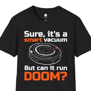 May include: Black t-shirt featuring a graphic of a smart vacuum cleaner and the text "Sure, it's a smart vacuum, But can it run DOOM?" in white and orange. The shirt has a crew neck.