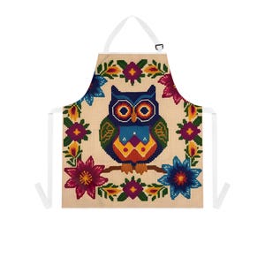 May include: A white kitchen apron featuring a colourful embroidered owl design. The owl is surrounded by flowers in shades of red, blue, yellow and green.